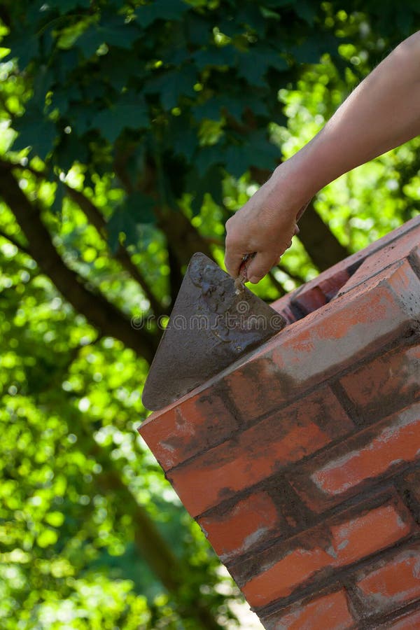 Mannetjeshand die werkt met een trowel die de schoorsteen van rode bakstenen op een dak van een landhuis herstelt