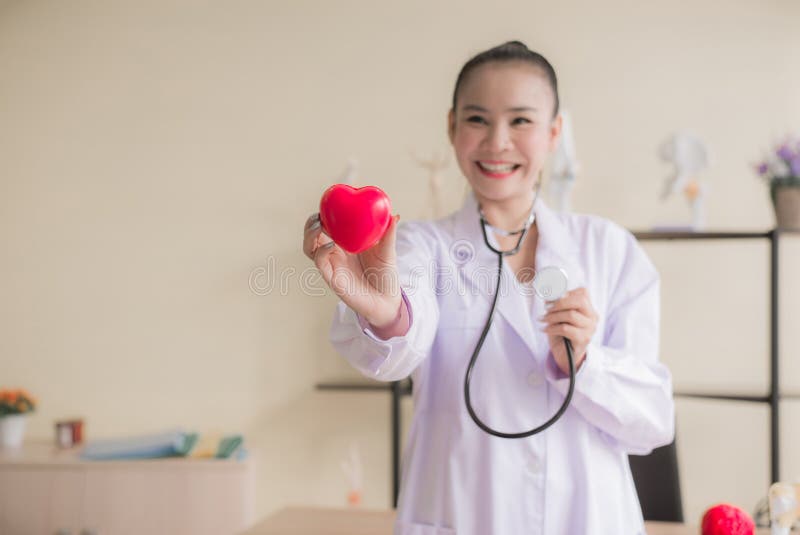 Mano asiática de la mujer del doctor que muestra a corazón de los instrumentos el modelo rojo, feliz y sonriendo, foco selectivo fotografía de archivo libre de regalías Mano asiática de la mujer del doctor que muestra a corazón de los instrumentos el modelo rojo, feliz y sonriendo, foco selectivo fotografía de archivo libre de regalías