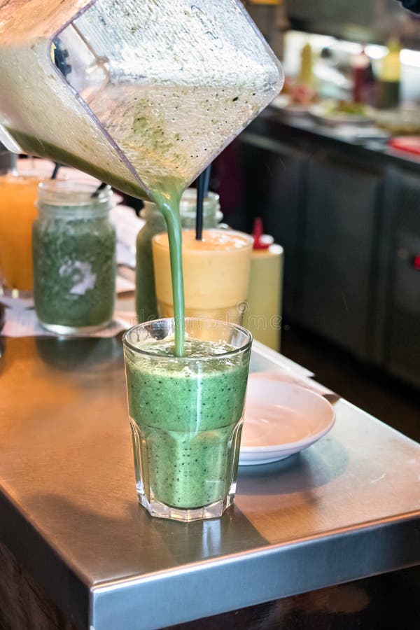 Mano che versa una forma smoothy di verdure della disintossicazione verde un miscelatore ad un vetro trasparente fotografie stock Mano che versa una forma smoothy di verdure della disintossicazione verde un miscelatore ad un vetro trasparente fotografie stock
