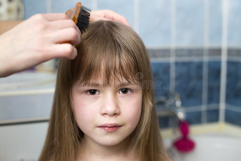 Mother hand with brush combing long fair hair of cute child girl after bath on blurred interior background. Mother hand with brush combing long fair hair of cute child girl after bath on blurred interior background.