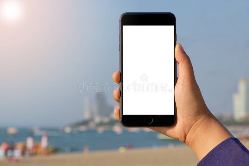 Mano de la mujer del primer que sostiene el teléfono móvil en fondo del arena de mar fresca hermosa y del cielo azul fotos de archivo libres de regalías Mano de la mujer del primer que sostiene el teléfono móvil en fondo del arena de mar fresca hermosa y del cielo azul fotos de archivo libres de regalías