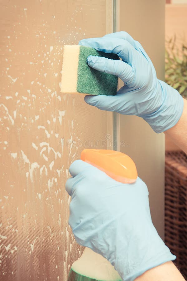 Mano de la mujer mayor que usa la esponja con el detergente para la ducha de cristal que se lava y de limpieza imágenes de archivo libres de regalías Mano de la mujer mayor que usa la esponja con el detergente para la ducha de cristal que se lava y de limpieza imágenes de archivo libres de regalías