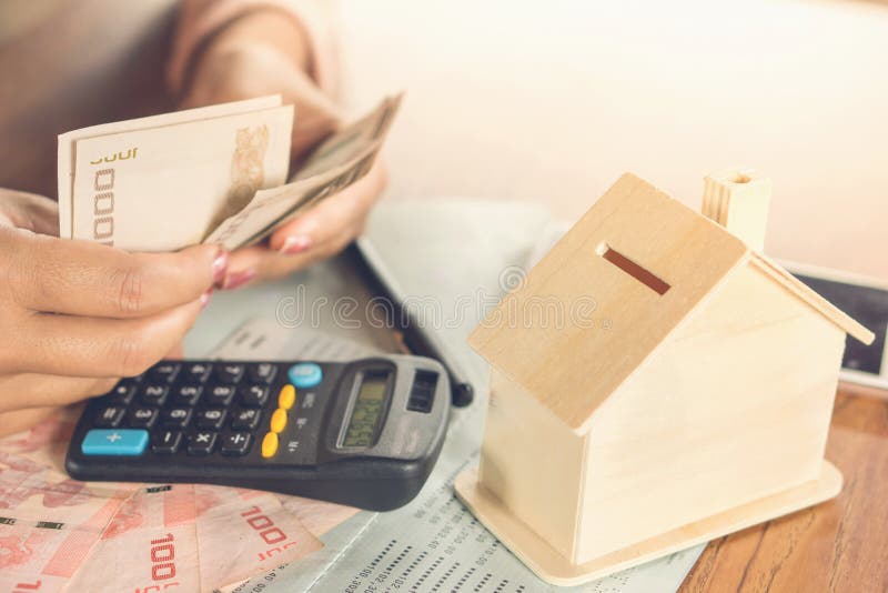 Mano de la mujer de negocios que cuenta el billete del dinero con el libro de cuentas de ahorro, el modelo de la casa y la calcul fotografía de archivo Mano de la mujer de negocios que cuenta el billete del dinero con el libro de cuentas de ahorro, el modelo de la casa y la calcul fotografía de archivo