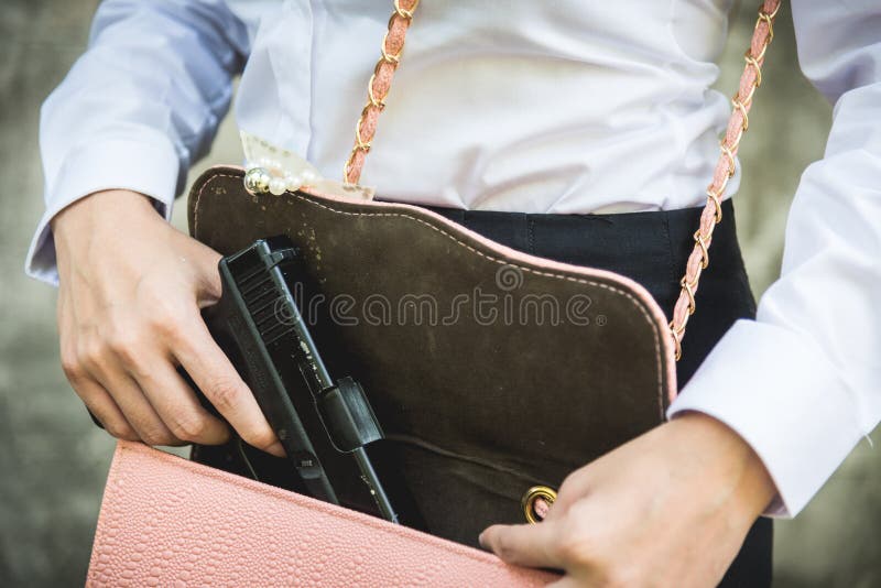 Mano de la mujer que celebra la eliminación de la pequeña arma de mano de su monedero foto de archivo libre de regalías Mano de la mujer que celebra la eliminación de la pequeña arma de mano de su monedero foto de archivo libre de regalías