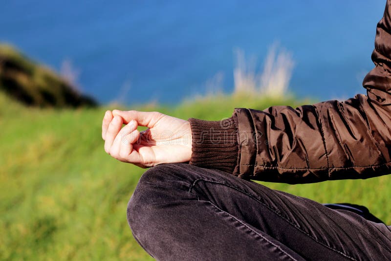 Mano de la mujer que medita en actitud de la yoga encima de los acantilados en la primavera en la puesta del sol fotografía de archivo libre de regalías Mano de la mujer que medita en actitud de la yoga encima de los acantilados en la primavera en la puesta del sol fotografía de archivo libre de regalías