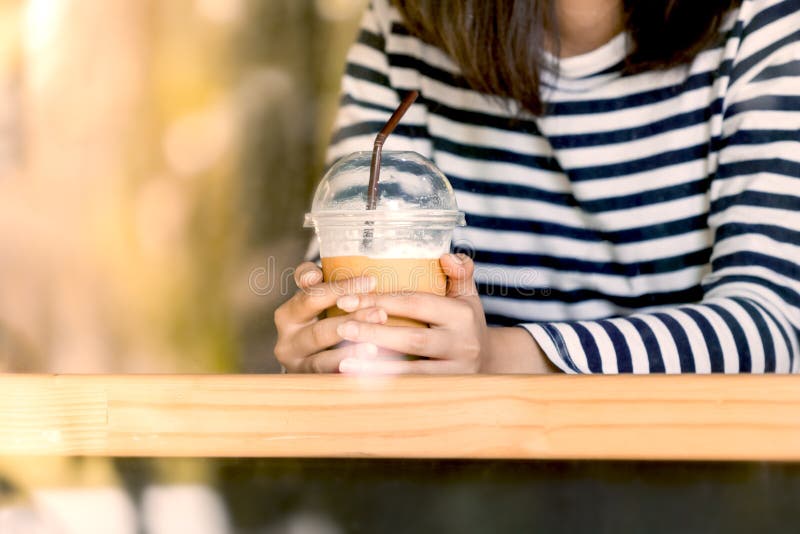 Mano de la mujer que sostiene la taza plástica de café de hielo en el café imagenes de archivo Mano de la mujer que sostiene la taza plástica de café de hielo en el café imagenes de archivo