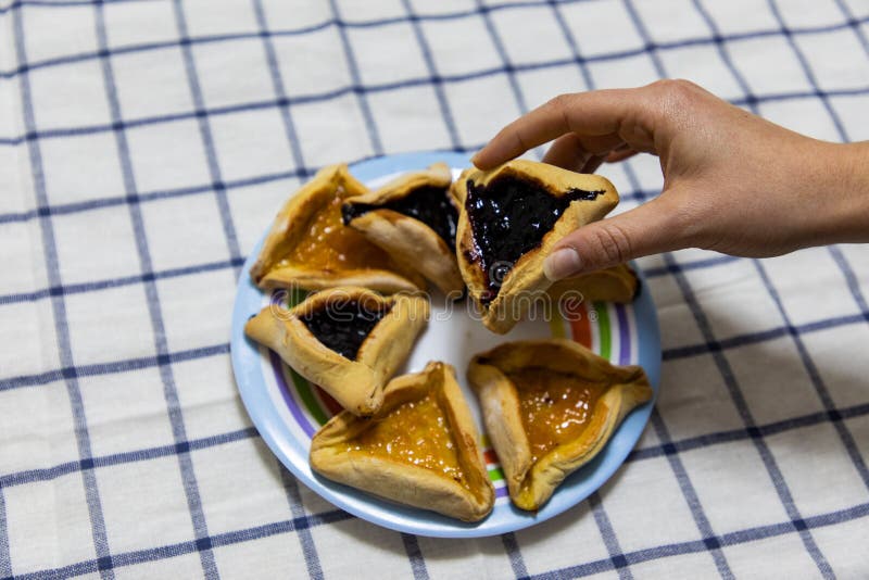 Mano de la mujer que sostiene las galletas del atasco del ar?ndano y del albaricoque de Hamantash Purim en la placa coloreada en imagen de archivo Mano de la mujer que sostiene las galletas del atasco del ar?ndano y del albaricoque de Hamantash Purim en la placa coloreada en imagen de archivo