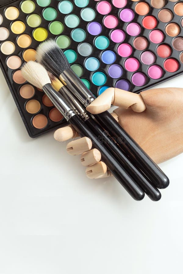 Mano de madera con los cepillos del maquillaje, maquillaje colorido del maniquí en blanco foto de archivo Mano de madera con los cepillos del maquillaje, maquillaje colorido del maniquí en blanco foto de archivo