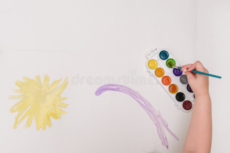 Mano del bambino con le spazzole che attingono il sole di giallo del Libro Bianco immagini stock Mano del bambino con le spazzole che attingono il sole di giallo del Libro Bianco immagini stock