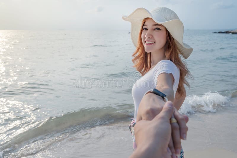Mano della tenuta della donna del suo ragazzo mentre conducendo alla spiaggia del mare immagine stock Mano della tenuta della donna del suo ragazzo mentre conducendo alla spiaggia del mare immagine stock