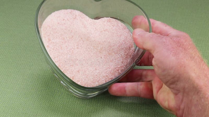 Mano derecha que muestra sal rosa himalaya de grano fino en un plato cardíaco