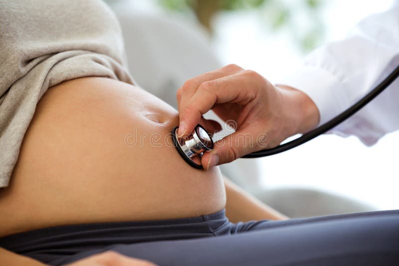 Mano di medico maschio dell'ostetrico con lo stetoscopio che ascolta il battito cardiaco del bambino della donna incinta