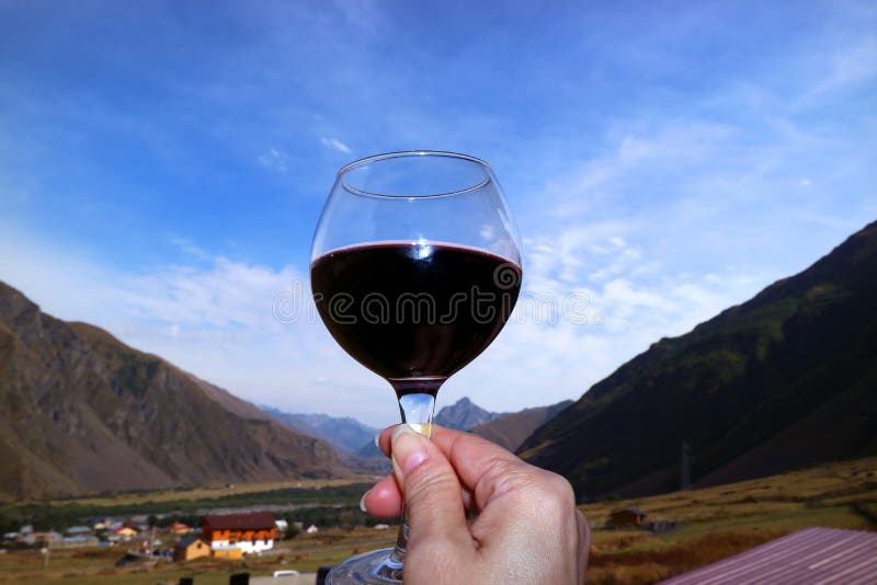 Mano di una donna che tiene un bicchiere di vino rosso contro il cielo azzurro fotografie stock libere da diritti Mano di una donna che tiene un bicchiere di vino rosso contro il cielo azzurro fotografie stock libere da diritti