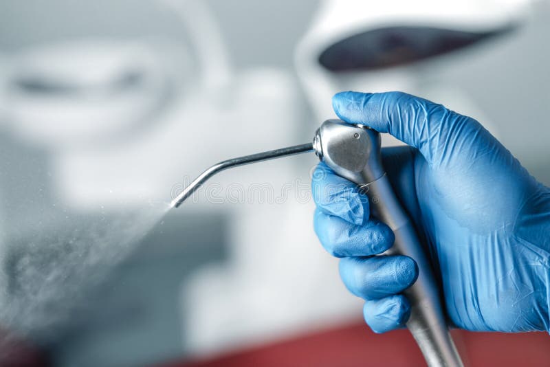 Mano femenina de dentista en guantes azules con jeringa de agua de aire, fondo borroso de clínica con unidad dental, odontología