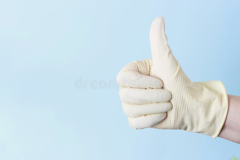 Mano femenina en los guantes blancos de goma con aumentado para arriba su pulgar en un fondo azul foto de archivo Mano femenina en los guantes blancos de goma con aumentado para arriba su pulgar en un fondo azul foto de archivo
