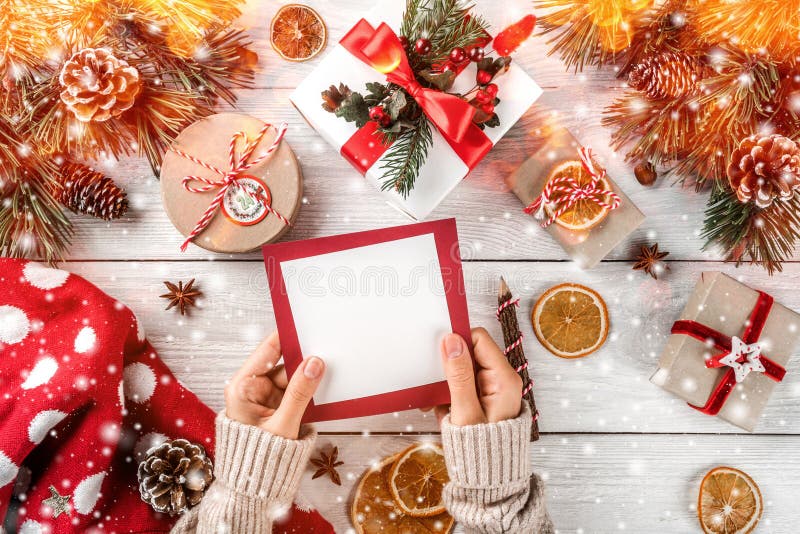 Mano femminile che scrive una lettera a Santa sul fondo di legno bianco con i regali di Natale, rami dell'abete, maglione, pigne fotografie stock Mano femminile che scrive una lettera a Santa sul fondo di legno bianco con i regali di Natale, rami dell'abete, maglione, pigne fotografie stock