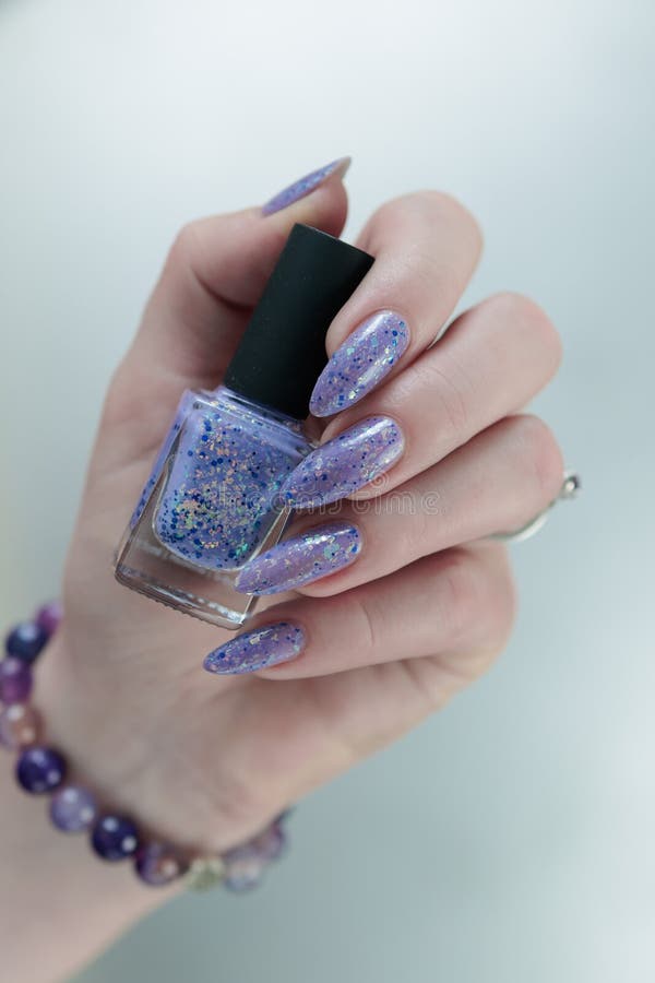 Mano hembra con uñas largas y lila color púrpura esmalte de uñas. Mano hembra con uñas largas y una botella de lilo color púrpura esmalte de uñas