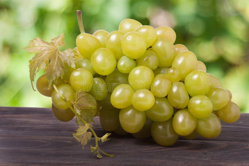 Manojo de uvas verdes maduras en una tabla de madera con el fondo borroso foto de archivo