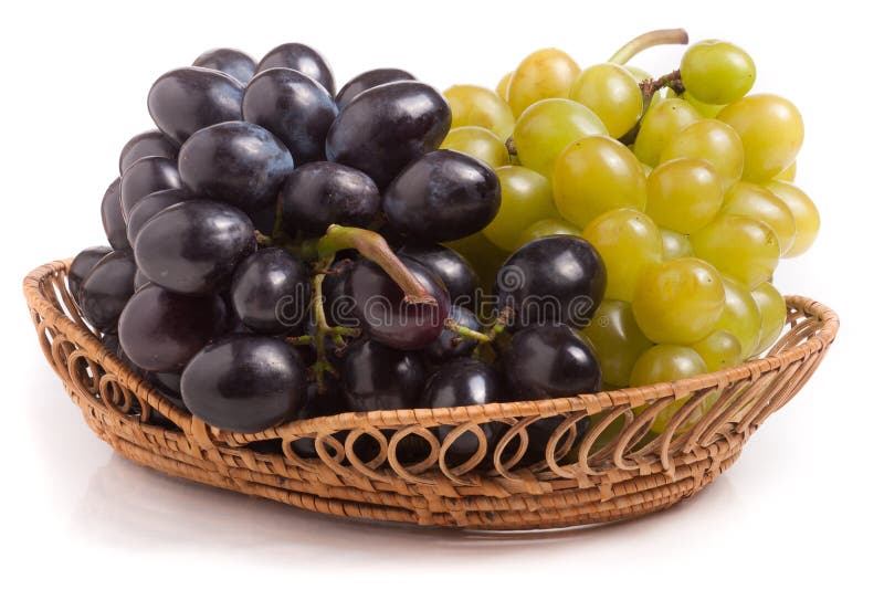 Manojo de uvas verdes y azules en la cesta de mimbre aislada en el fondo blanco foto de archivo