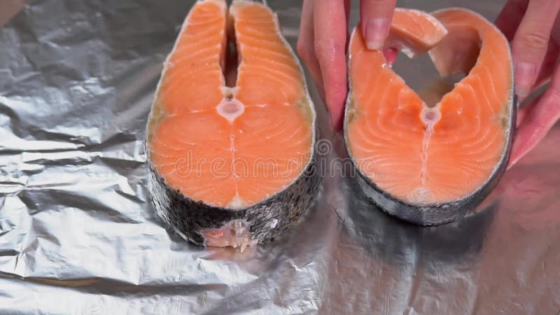 Manos de chicas poniéndose el filete de salmón en la hoja para hornear. una mano pone un filete de salmón fresco en una hoja de co metrajes