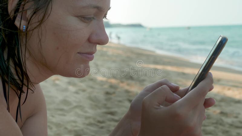 Manos de hembras con smartphone negro de fondo del agua de mar.