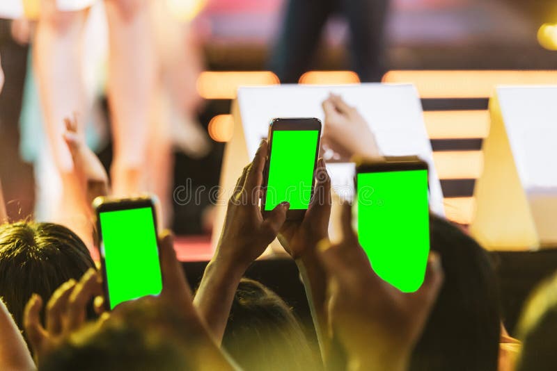 Manos de la gente de la muchedumbre de la audiencia que toma la foto con el teléfono elegante móvil con la pantalla verde en conc fotografía de archivo libre de regalías Manos de la gente de la muchedumbre de la audiencia que toma la foto con el teléfono elegante móvil con la pantalla verde en conc fotografía de archivo libre de regalías