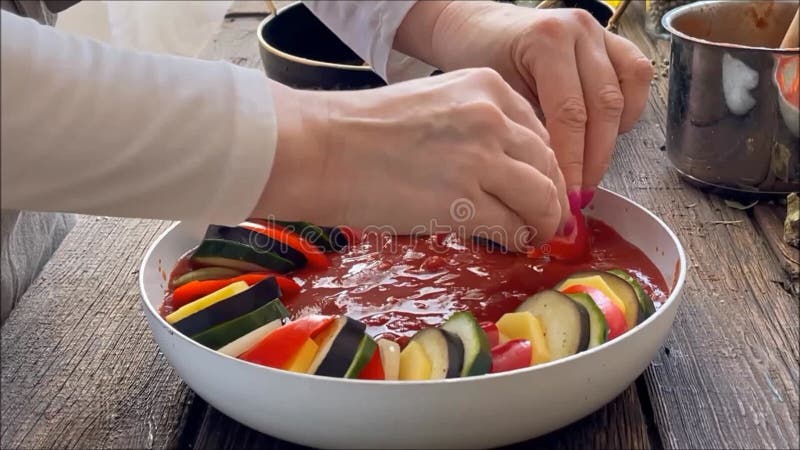 Manos de mujeres ponen verduras cortadas en un bol con salsa de tomate. preparación de platos de ratatouille