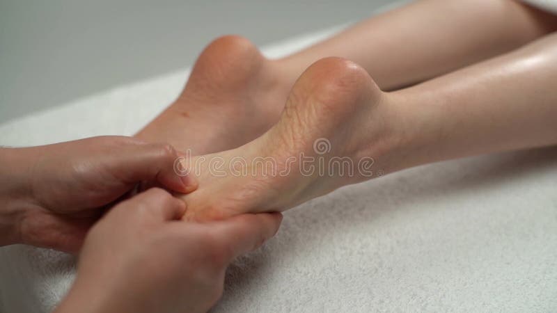 Estrechar las manos de los pies masajeadores masculinos a una joven tendida sobre una mesa de masaje en el salón de spa.