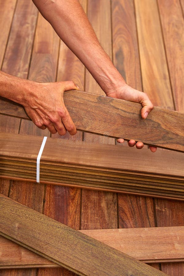 Manos del carpintero de la instalación de la cubierta del Ipe que sostienen la madera fotografía de archivo Manos del carpintero de la instalación de la cubierta del Ipe que sostienen la madera fotografía de archivo
