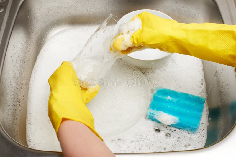Manos en los guantes amarillos que lavan el vidrio contra fregadero de cocina fotos de archivo Manos en los guantes amarillos que lavan el vidrio contra fregadero de cocina fotos de archivo
