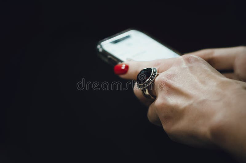 Female hands with a manicure and a ring hold the phone on a black background. Close-up, selective focus. Female hands with a manicure and a ring hold the phone on a black background. Close-up, selective focus.