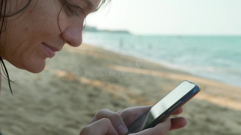 Manos femeninas usando smartphone negro sobre fondo de agua de mar