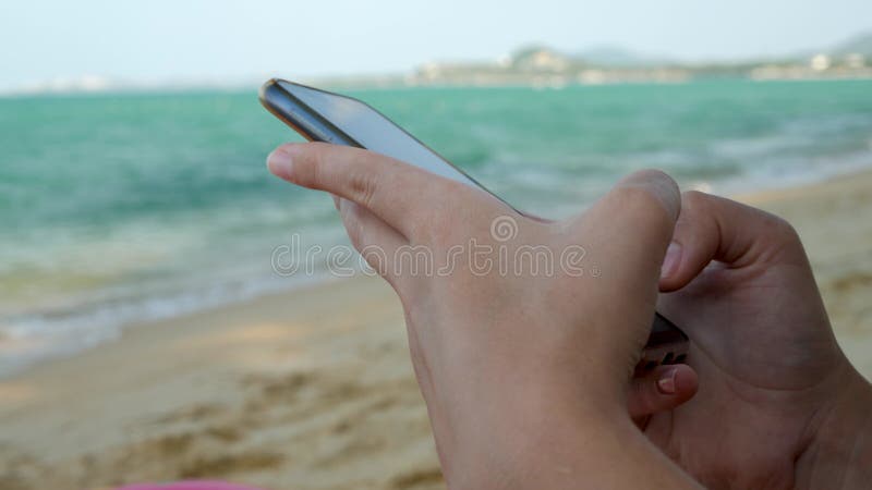 Manos femeninas usando smartphone negro sobre fondo de agua de mar