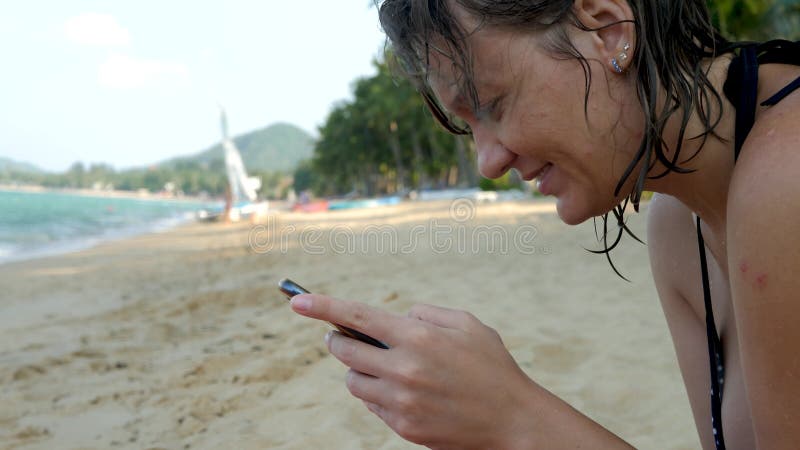 Manos femeninas usando smartphone negro sobre fondo de agua de mar