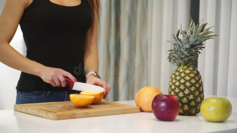 Manos hembras cortando naranja en una tabla de madera. mujer en la cocina. alimentación saludable. alimento crudo.