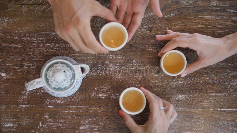 Manos humanas que toman las tazas de té de la tabla rústica de madera y que beben la opinión de ceremonia de té de verde del chin