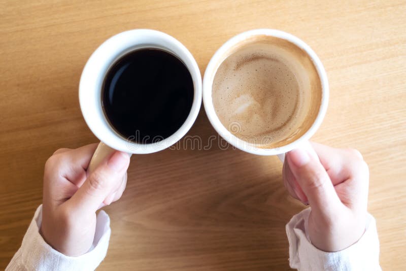 Manos que sostienen dos tazas de café blancas en la tabla de madera en café fotografía de archivo Manos que sostienen dos tazas de café blancas en la tabla de madera en café fotografía de archivo