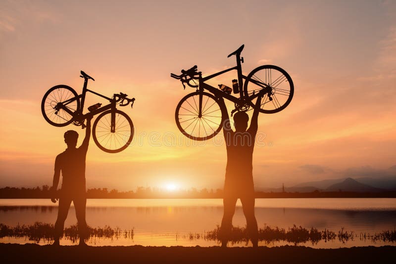Manställning för kontur två i handlinglyftande cykel ovanför hans huvud på solnedgång arkivbilder Manställning för kontur två i handlinglyftande cykel ovanför hans huvud på solnedgång arkivbilder