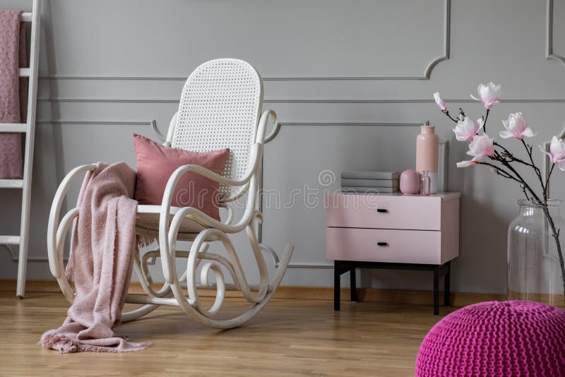 Manta rosada en colores pastel y almohada en la mecedora blanca en sitio sofisticado con el nightstand y las flores en el florero