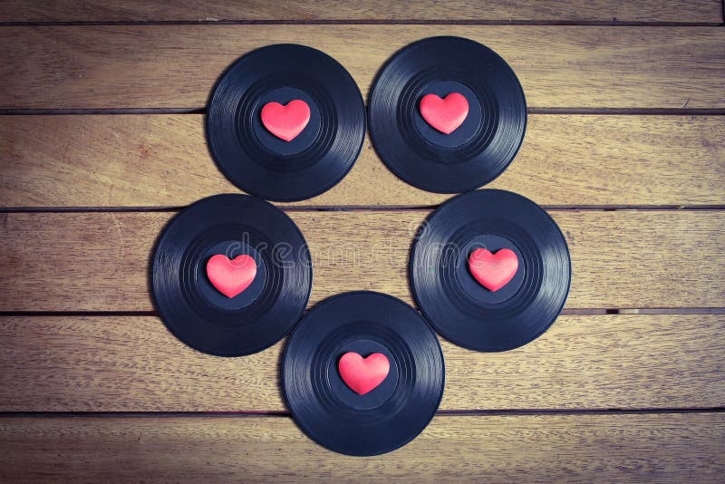 Vinyl records with red love hearts in a circular pattern on a wooden surface. Vinyl records with red love hearts in a circular pattern on a wooden surface