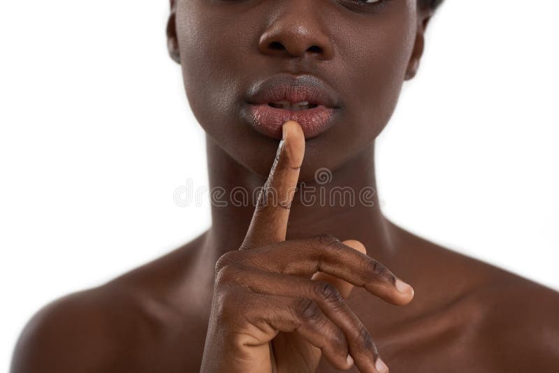 Mantendo um segredo. foto cortada de uma mulher africana sensual, dedo nos seus lábios inteiros enquanto estava de pé imagem de stock