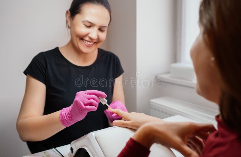 Manucure souriante spécialiste femelle appliquant le vernis à ongles de base. Salon de beauté autosoin procédure agréable pour le photo libre de droits