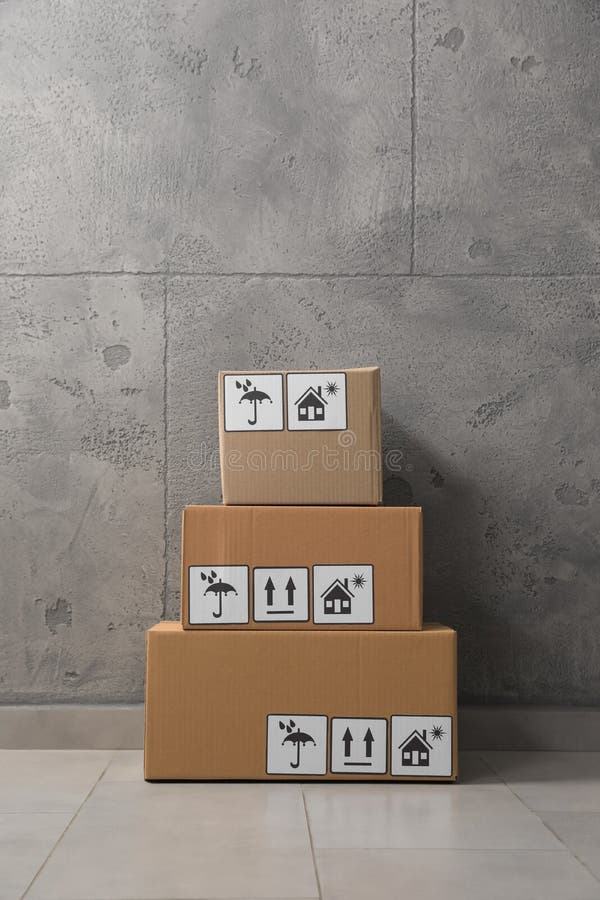 Many Closed Cardboard Boxes with Packaging Symbols on Floor Near Grey