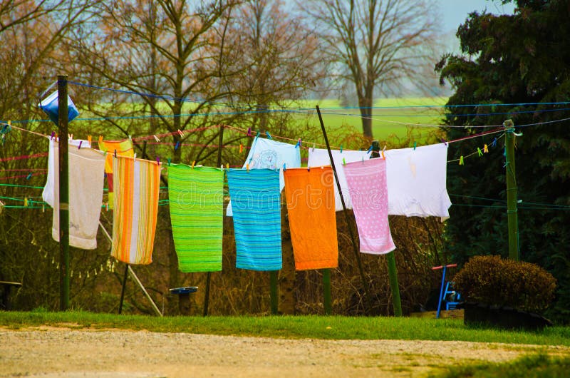 Many colorful towels, laundy are hanging on a clothing line in a county yard of an old farmhouse. In springtime