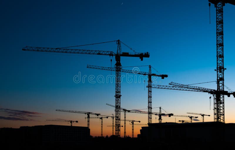many construction cranes on sunset sky , crane silhouette skyline