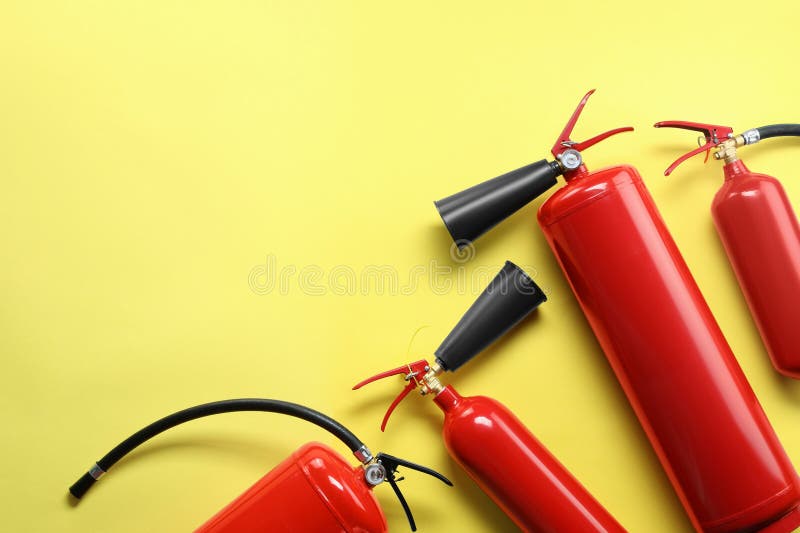 Many fire extinguishers on yellow background, flat lay. Space for text stock photography