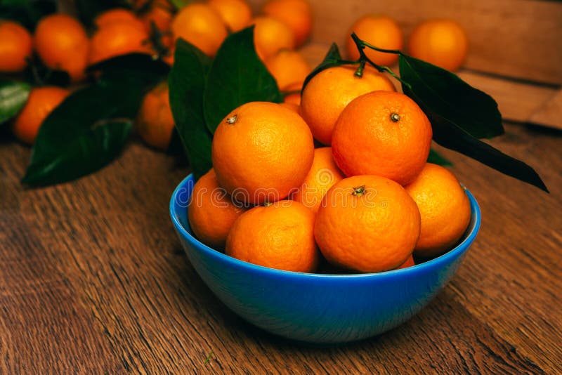 Many Fresh Mandarin Oranges in Blue Bowl, Standing on a Wooden Table Blurred Background Stock