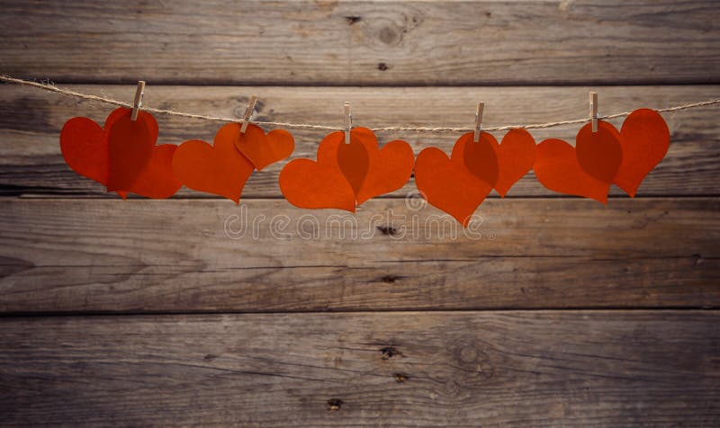 Red paper hearts hangs on clothespins on a wooden background. Red paper hearts hangs on clothespins on a wooden background