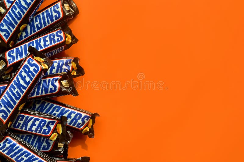 Many Snickers chocolate bars lies on pastel orange paper. Snickers bars are produced by Mars Incorporated. Snickers was created by