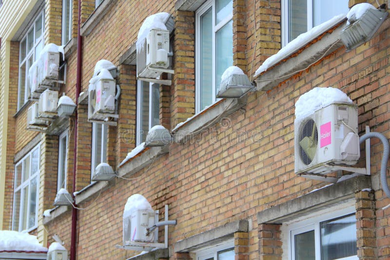 Many white air conditioning part of a split system hanging on a brick wall of a building covered in snow and icicles in winter in Russia